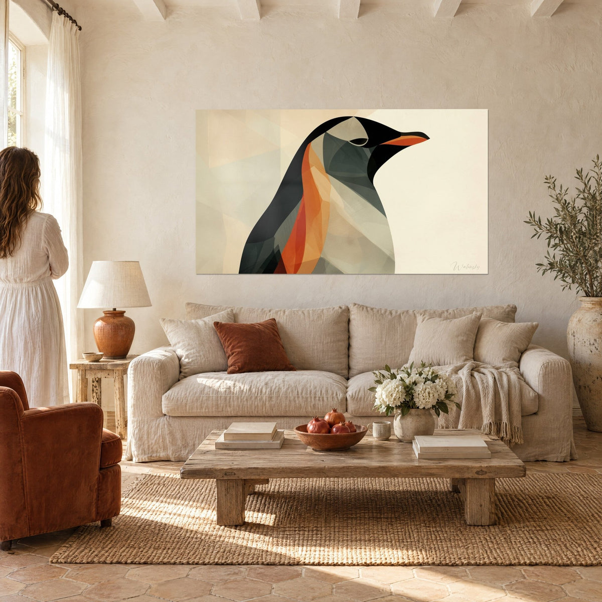 Gemälde Pinguin anthrazit mit orangefarbenem Schnabel, kupferfarbene Strähnen auf cremefarbenem Hintergrund, eine Frau von hinten, über einem Sofa in einem hellen Wohnzimmer