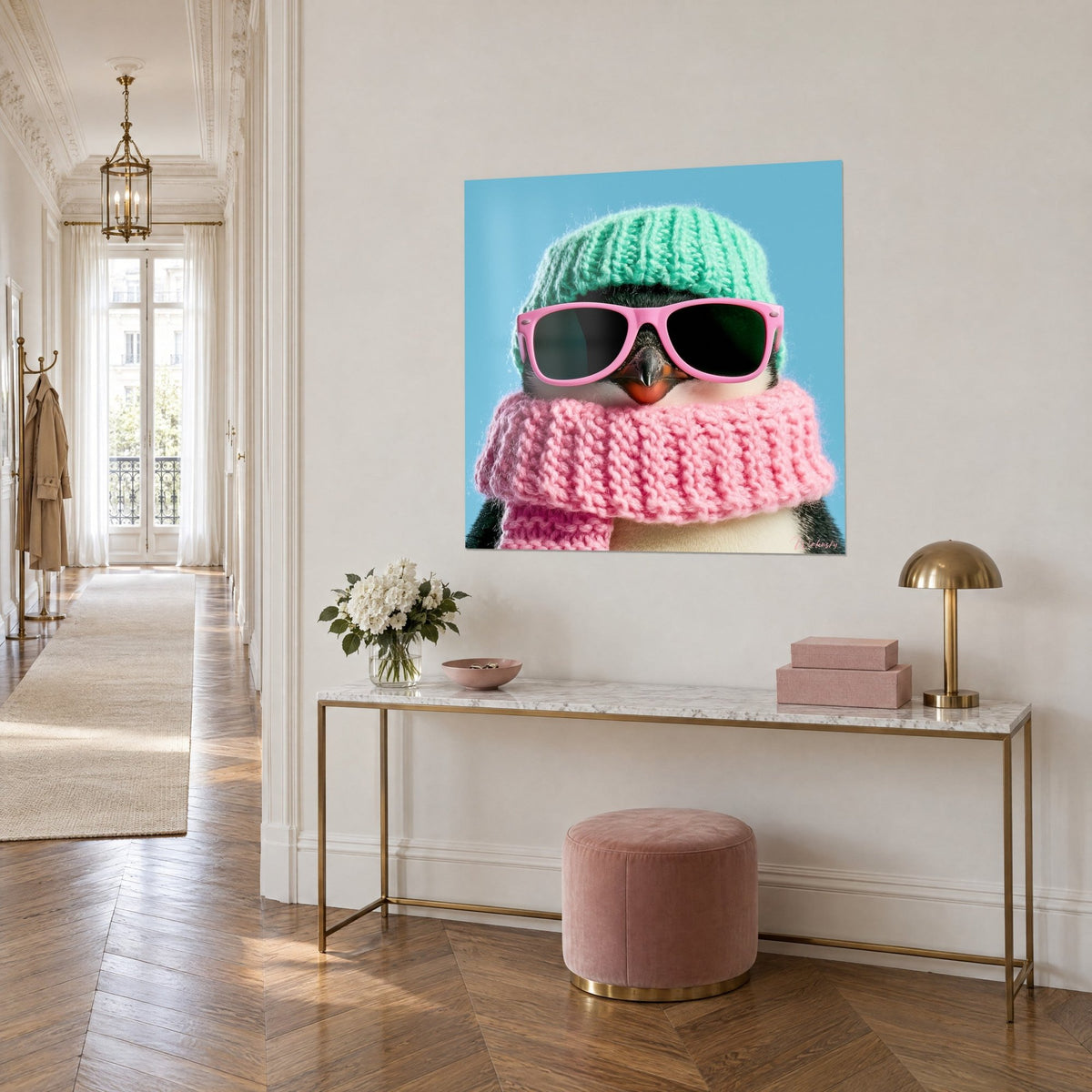 Schilderij van een lachende pinguïn met dikke bubblegumroze sjaal en groene muts, op een crèmekleurige muur boven een gouden consoletafel