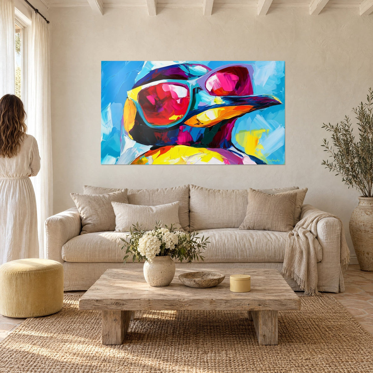 Tableau pingouin à lunettes de soleil roses, bec orange en larges coups de couteau sur fond bleu ciel, au-dessus d'un canapé dans un salon lumineux
