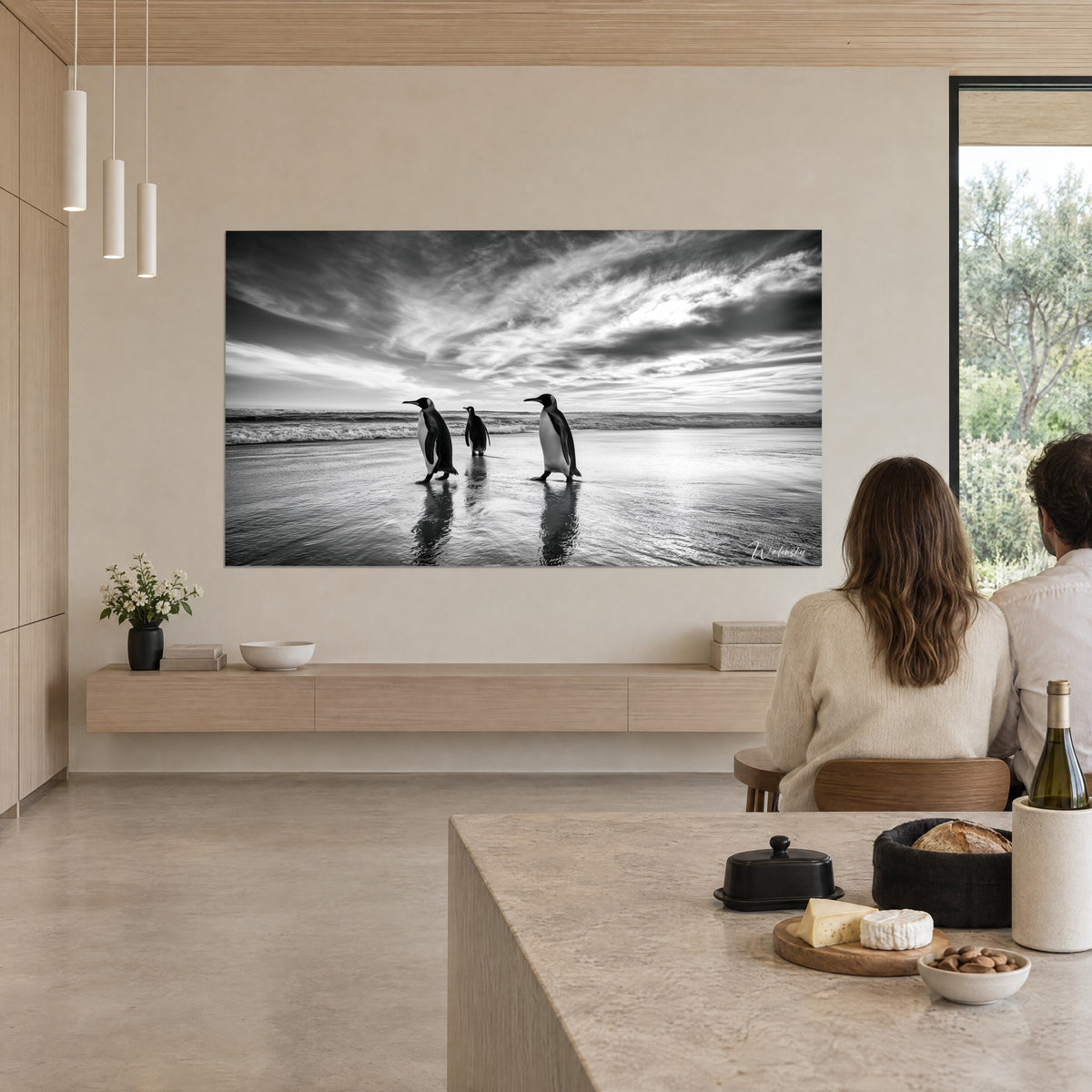 Tableau oiseaux de mer au plumage noir et blanc avançant vers l'écume, ciel gris strié, un couple de dos regarde depuis la cuisine ouverte