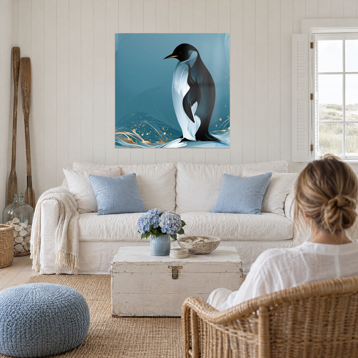 Tableau manchot à plastron blanc et dos noir sur fond bleu pétrole, vagues dorées en bas, au-dessus d'un canapé dans un salon lumineux