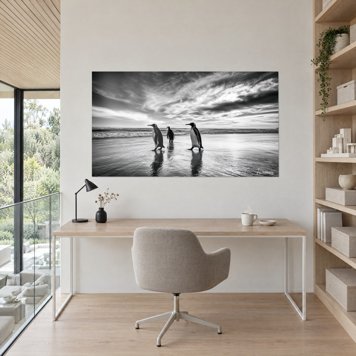 Tableau silhouettes de manchots en reflet sur le sable humide, noir profond et blanc éclatant, au-dessus d'un bureau en bois clair