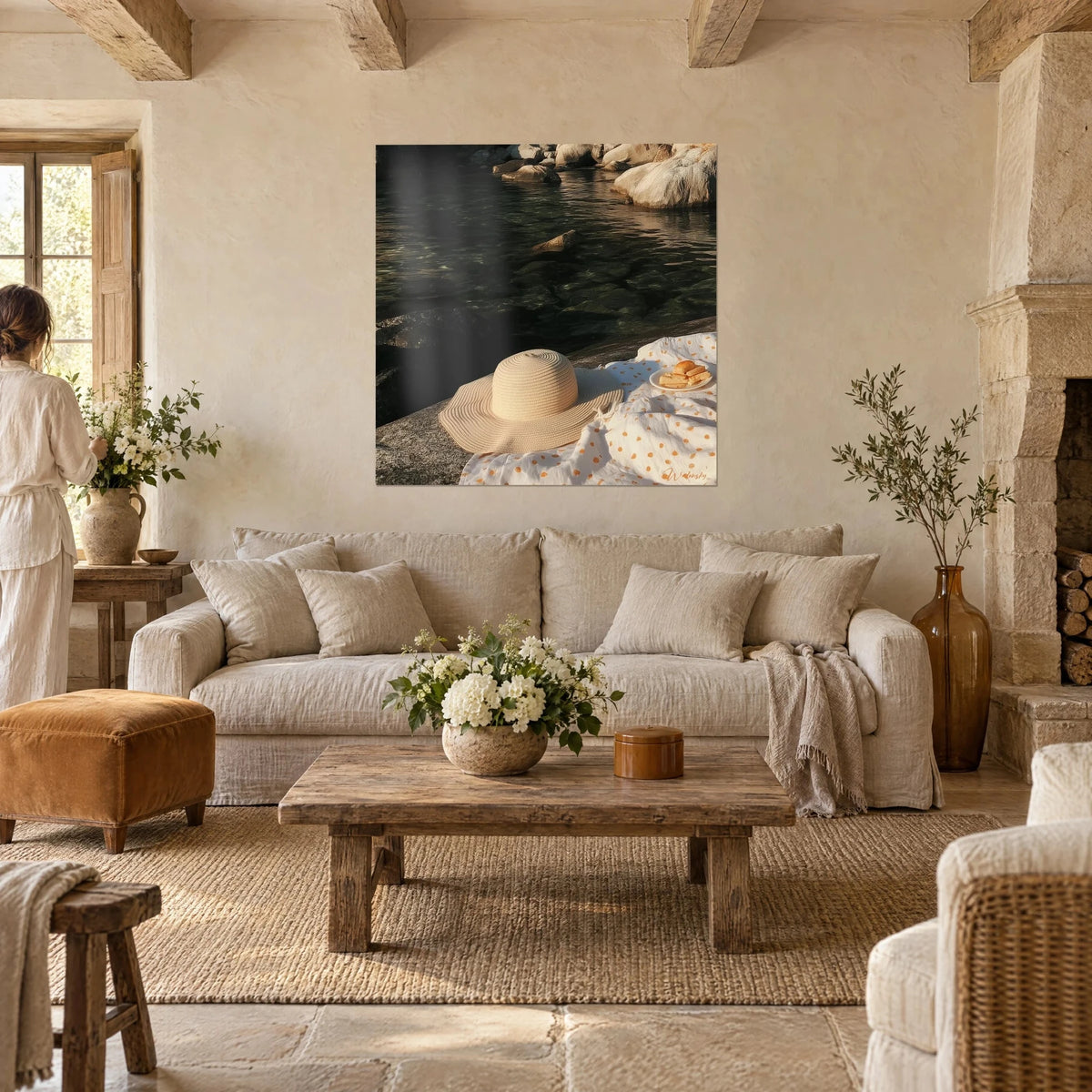 Wall art with beige straw hat on white blanket with orange polka dots, dark water and rocks, above a sofa in a bright living room
