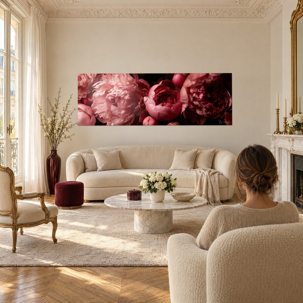 Cuadro peonías rosa pálido de pétalos arrugados sobre fondo negro, una mujer de espaldas, sobre un sofá en un salón luminoso