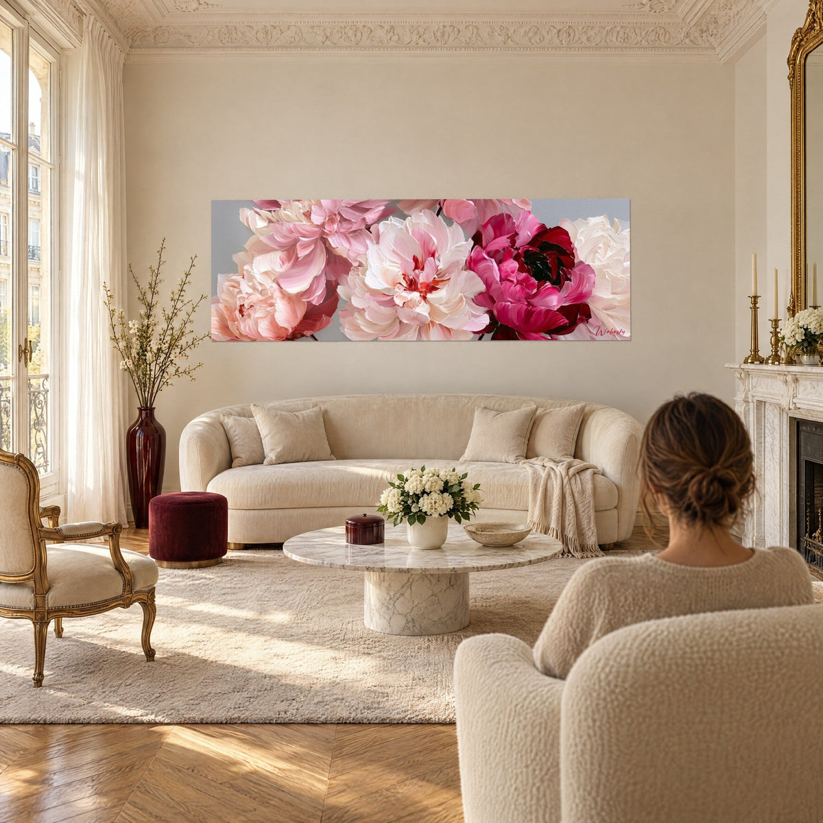 Wall art of a bouquet of open pink peonies, petals in ivory and crimson impasto, two people seen from behind above a sofa in a bright living room