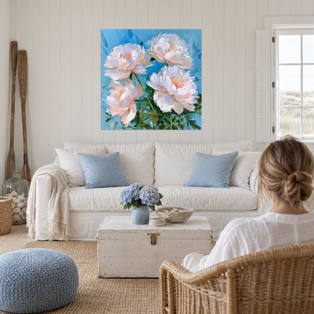 Wall art white peonies with orange stamens on a sky-blue background, two people seen from behind, above a sofa in a bright living room