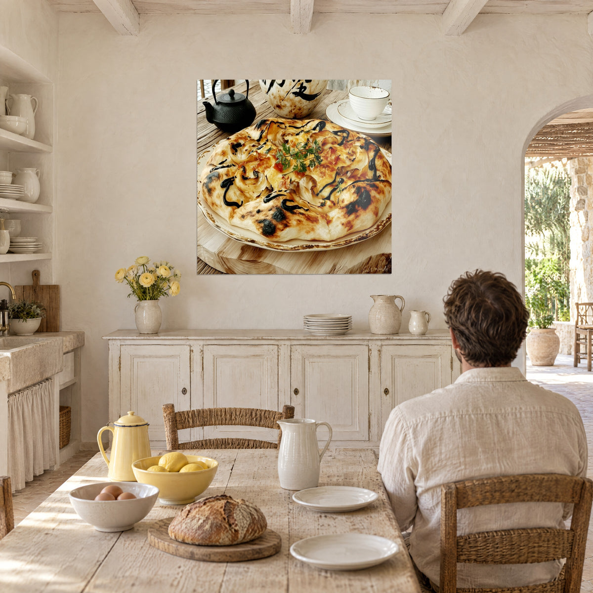 Tableau pain plat doré nappé de fromage fondu et de coulures noires, théière noire, cuisine claire d'un mas provençal