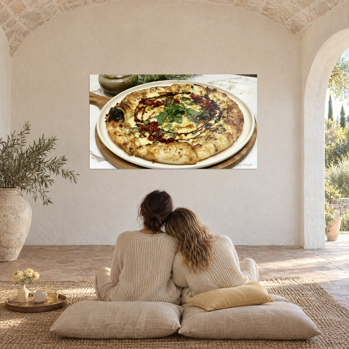 Tableau pizza croustillante couleur miel, herbes vertes et trait de glaçage sombre, couple enlacé de dos sur coussins, voûte blanche