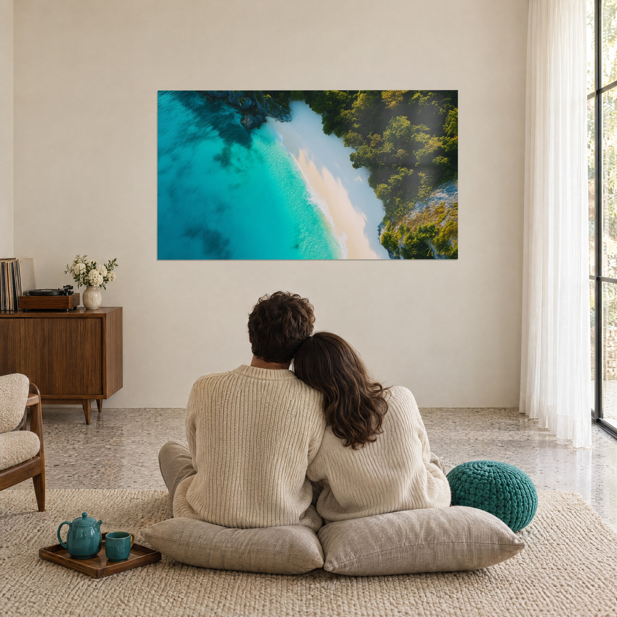 Tableau anse de sable blanc léchée par l'eau cyan et les arbres verts, devant un couple assis sur des coussins beiges