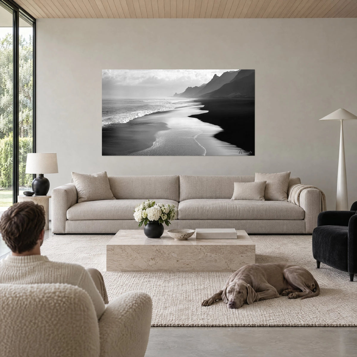 Wall art black sand beach edged with white foam, pearl-grey cliffs in the mist, above a sofa in a bright living room