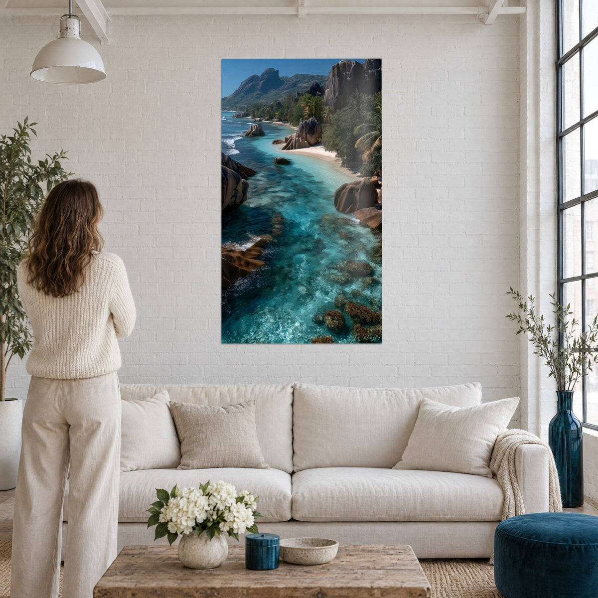 Tableau plage de sable blanc bordée de granit rose et d'eau turquoise, femme de dos, au-dessus d'un canapé dans un salon lumineux