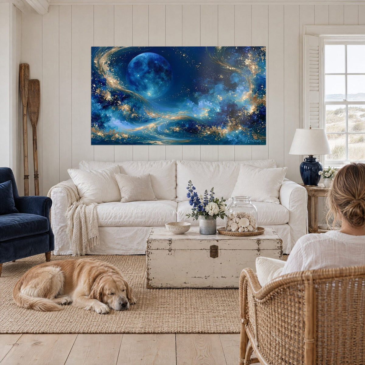 Tableau lune bleue cobalt aux volutes d'or tourbillonnantes, retriever couché et personne de dos, au-dessus d'un canapé dans un salon lumineux