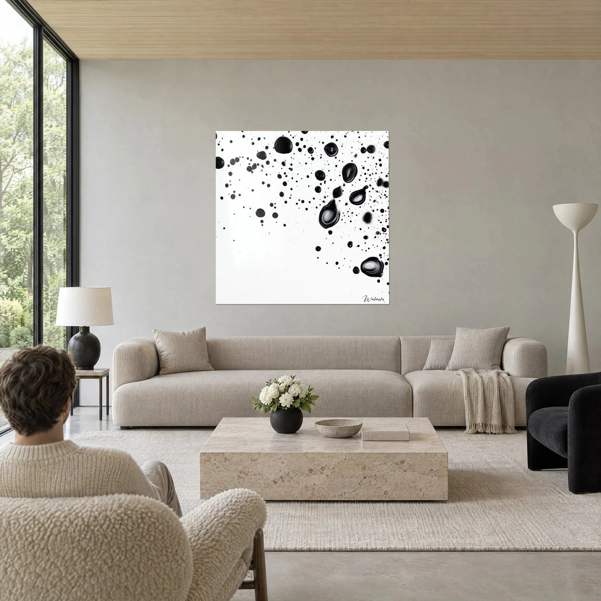 Cuadro de salpicaduras de tinta negra sobre fondo blanco, gotas brillantes arriba a la derecha, encima de un sofá en un salón luminoso