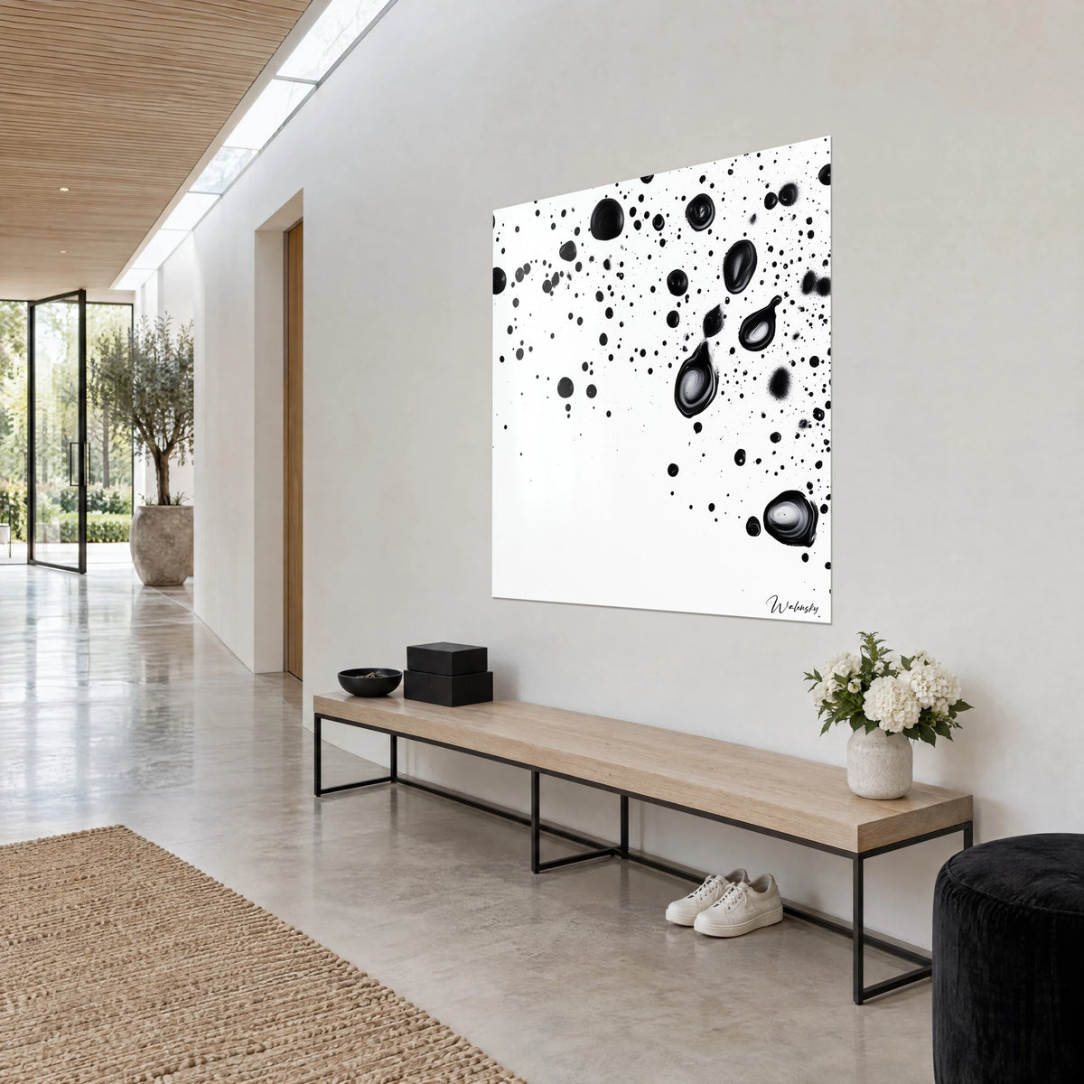 Cuadro de gotas de tinta negro ébano y finas salpicaduras sobre blanco puro, colgado en la pared de un pasillo claro, banco de madera debajo