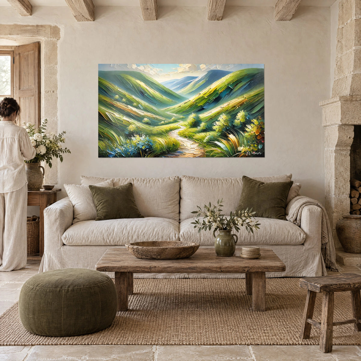 Wall art alpine valley with grass-green and ochre hills, cream winding path, woman seen from behind, above a sofa in a bright living room