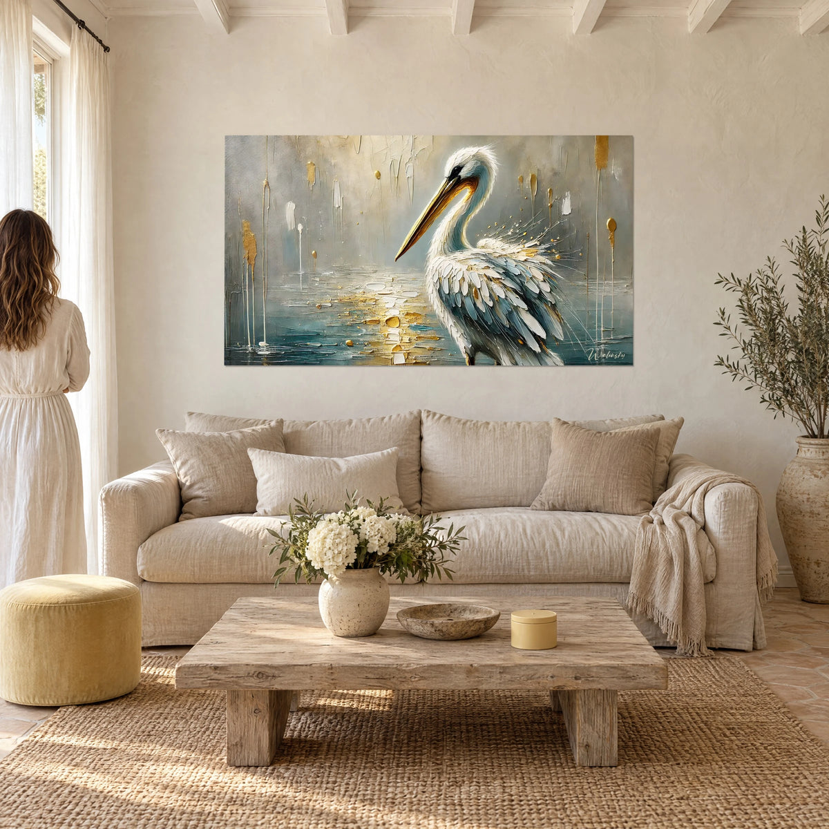 Schilderij van een witte pelikaan met lange gouden snavel, blauwgrijze veren op een zilveren achtergrond, boven een bank in een lichte woonkamer