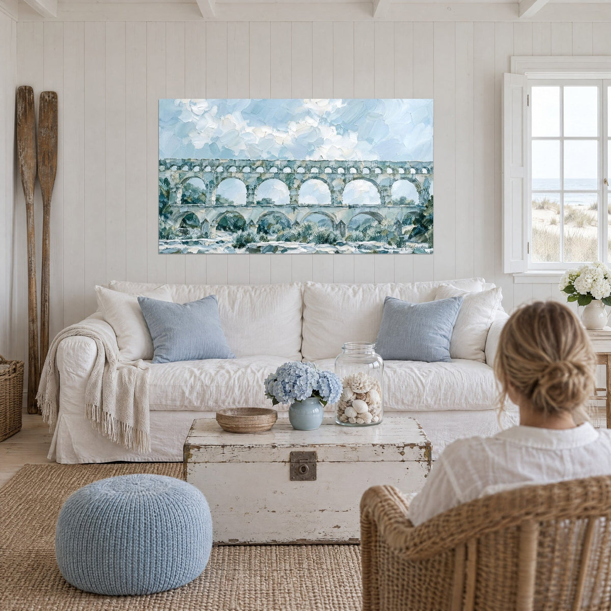 Gemälde römisches Aquädukt aus grauem Stein unter einem hellblauen Himmel, mit dem Spachtel gemalte Bögen, über einem Sofa in einem hellen Wohnzimmer