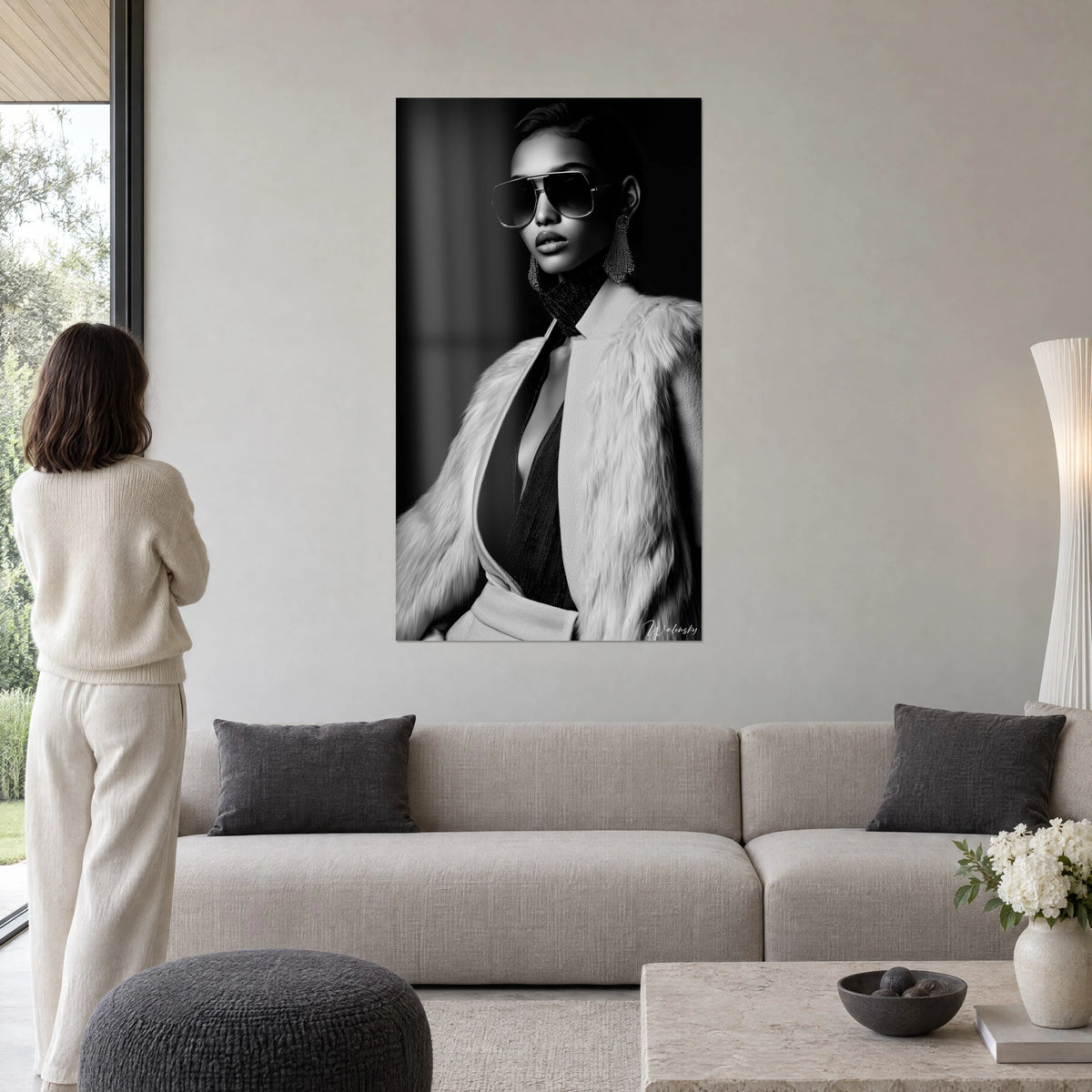 Cuadro modelo con gafas aviador y abrigo de piel marfil, en blanco y negro, encima de un sofá en un salón luminoso
