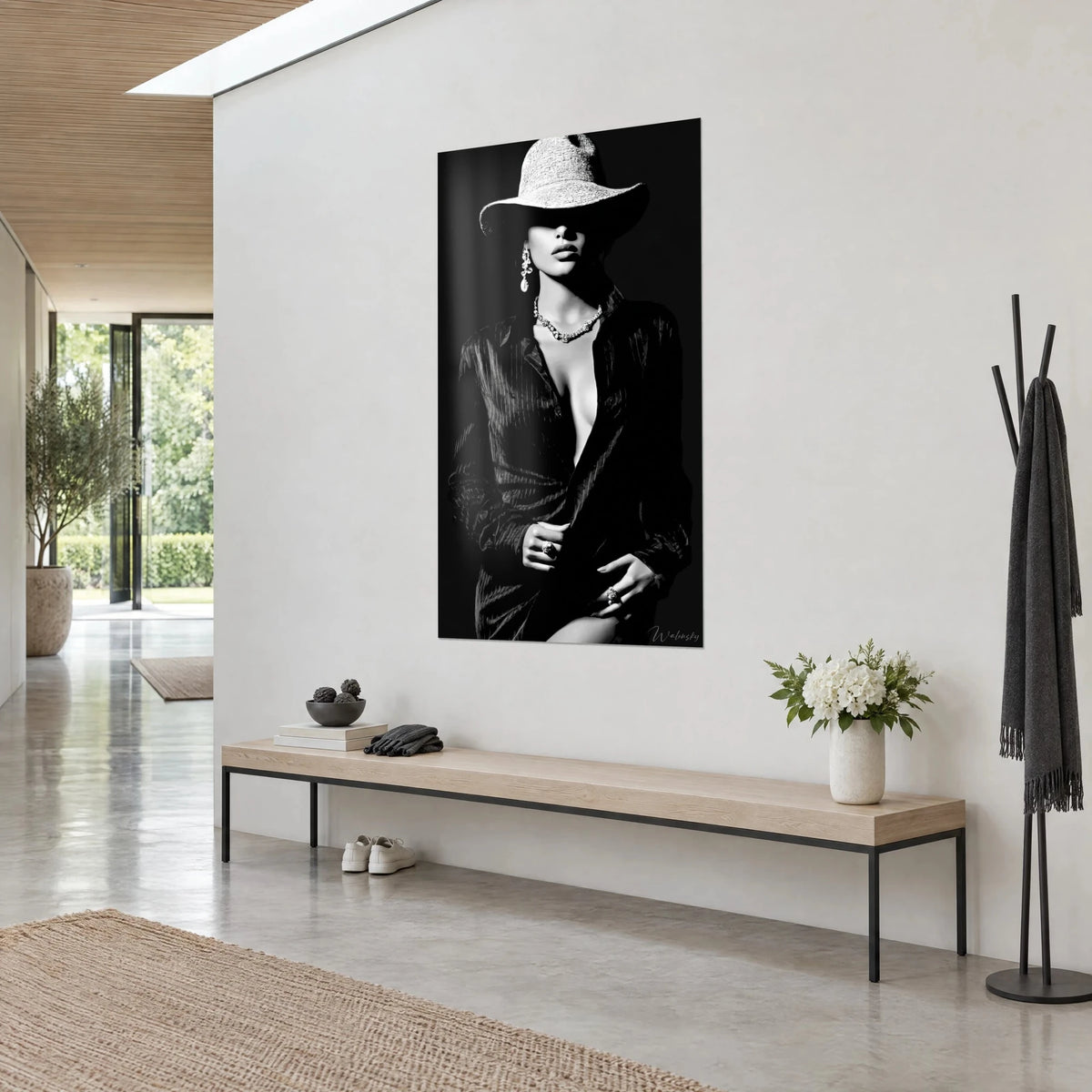 Quadro di una modella in bianco e nero, cappello a tesa larga, labbra carnose, collana con pietre e orecchino di perla, su un muro bianco di corridoio