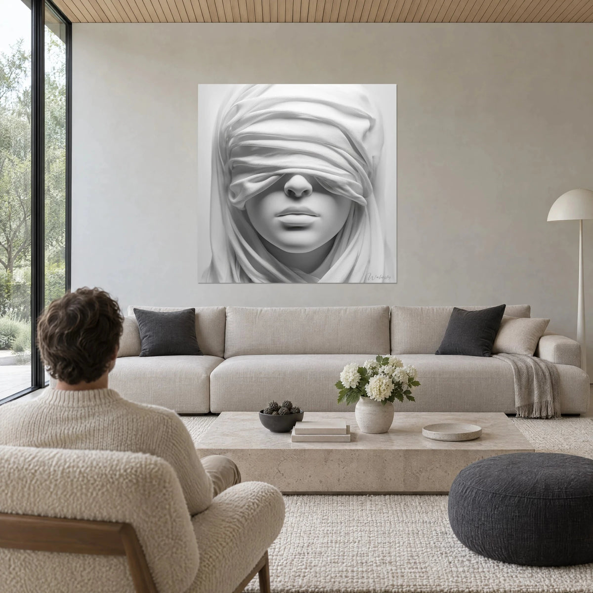 Wall art of a woman's face blindfolded with a crumpled white cloth, pearl grey shadows, above a sofa in a bright living room