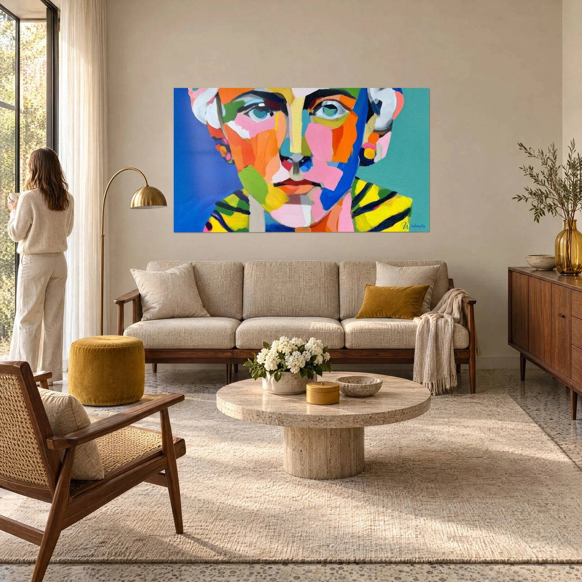 Gemälde kubistisches Gesicht mit rosa und orangefarbenen Flächen, türkisfarbene Augen, blauer Hintergrund, eine Frau von hinten, über einem Sofa in einem hellen Wohnzimmer