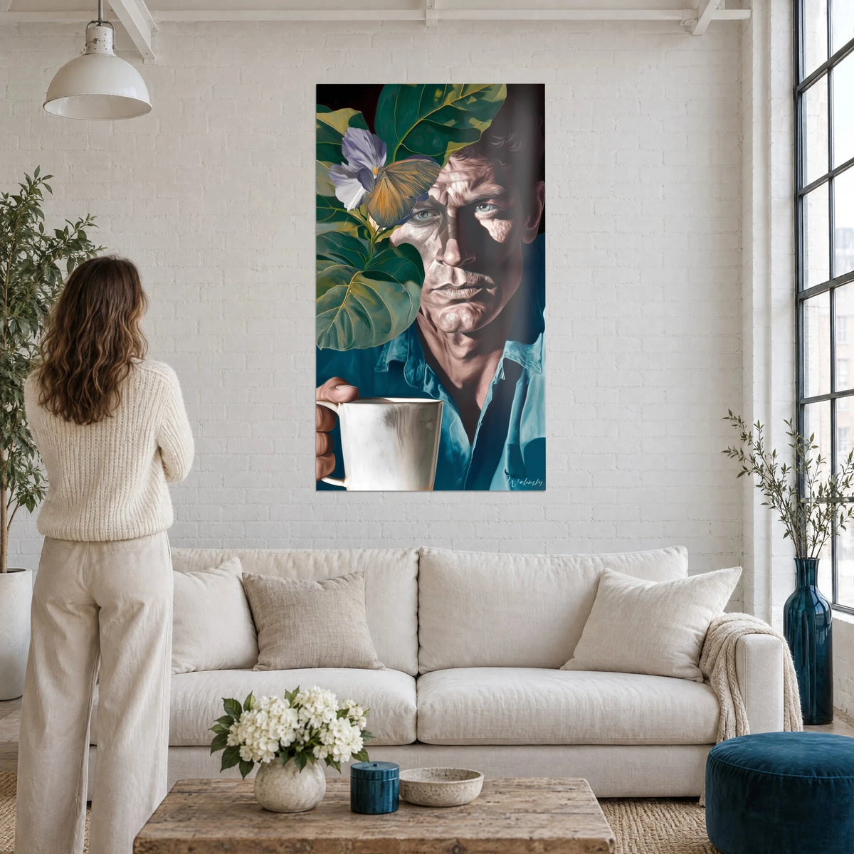 Tableau portrait d'homme au regard bleu glacier, feuilles vert sapin et papillon ocre, au-dessus d'un canapé dans un salon lumineux
