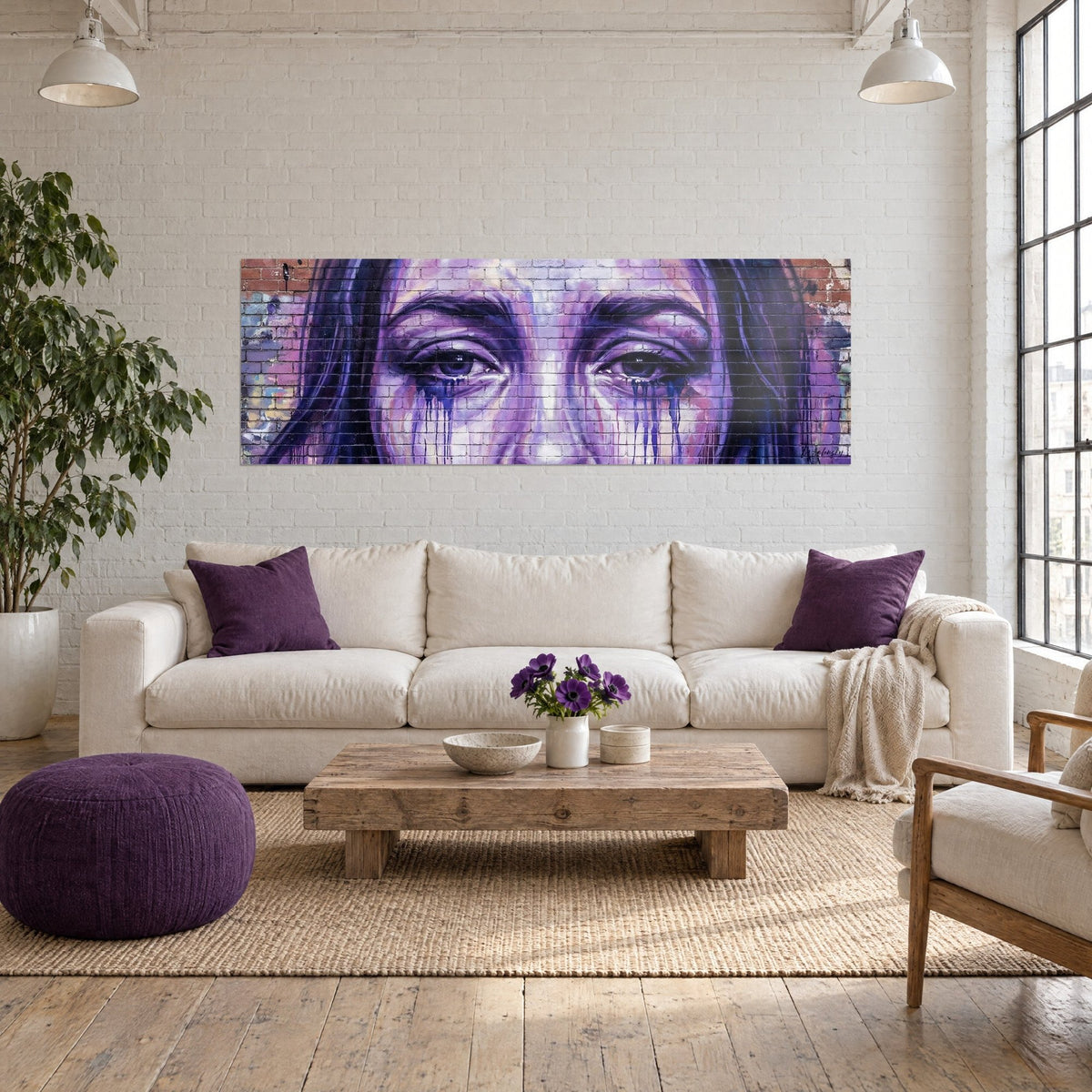 Wall art female gaze with blue tears, dark irises, purple and pink brick wall, hung above a sofa in a bright living room