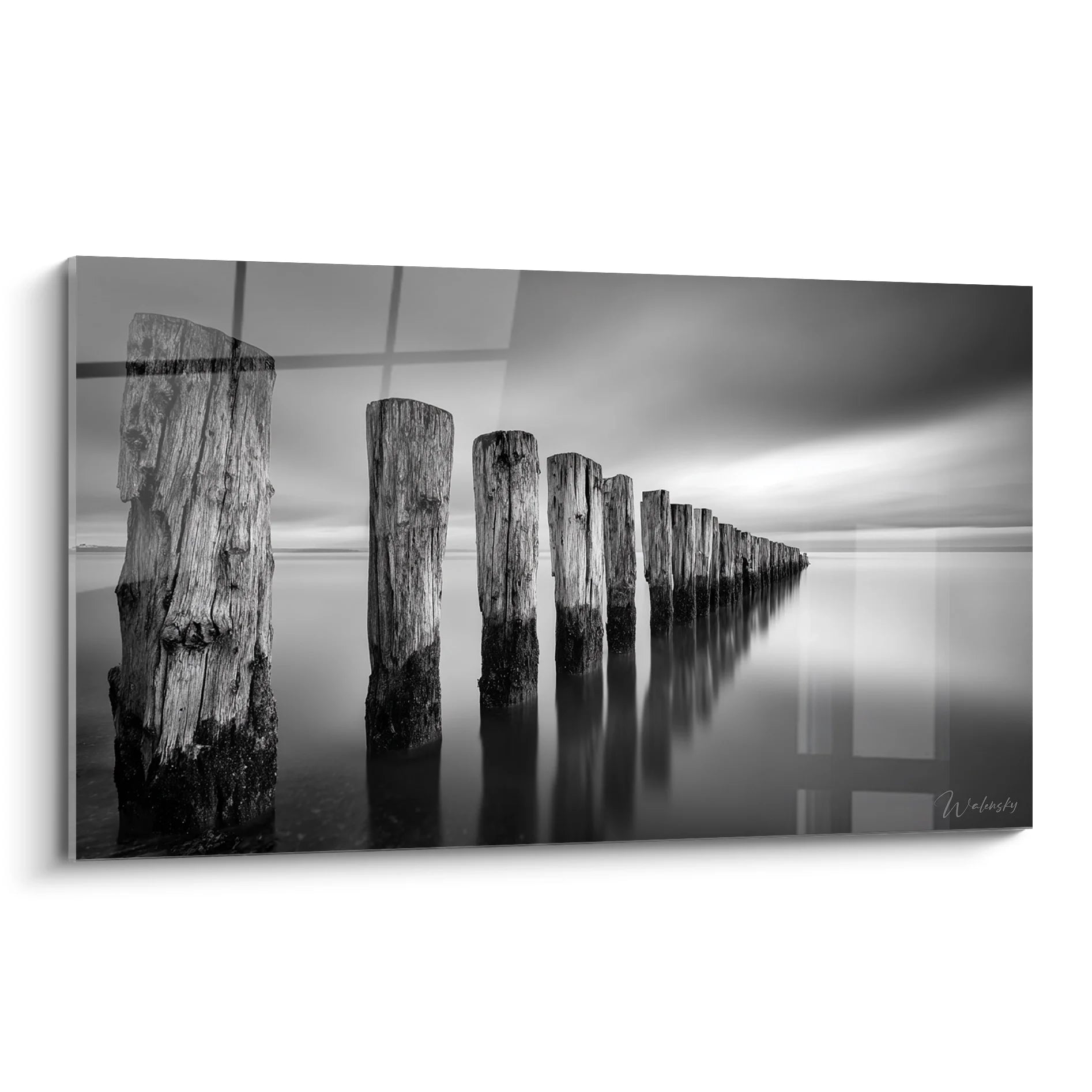 Tableau noir et blanc de poteaux en bois alignés dans l'eau calme avec reflets et ciel nuageux