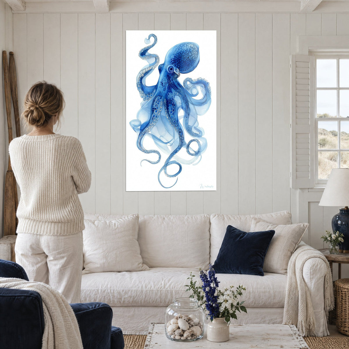 Cuadro pulpo índigo con ventosas enmarcadas en círculos, tentáculos de humo azul cielo, mujer de espaldas, encima de un sofá en un salón luminoso