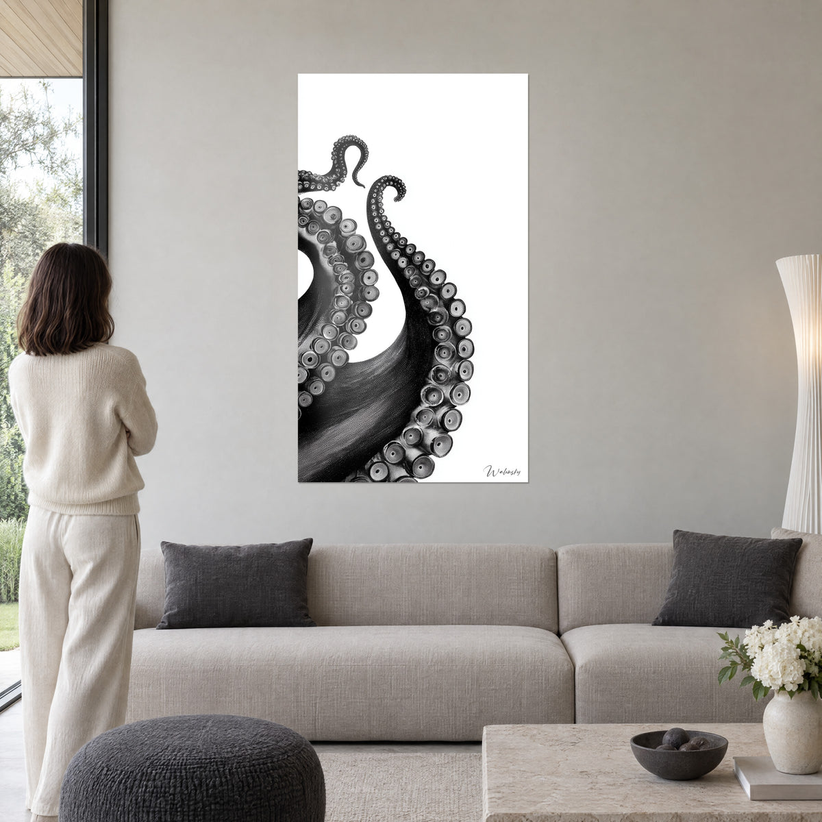 Schilderij zwarte octopusarmen met spiraalvormige zuignappen op witte achtergrond, vrouw van achteren, boven een bank in een lichte woonkamer