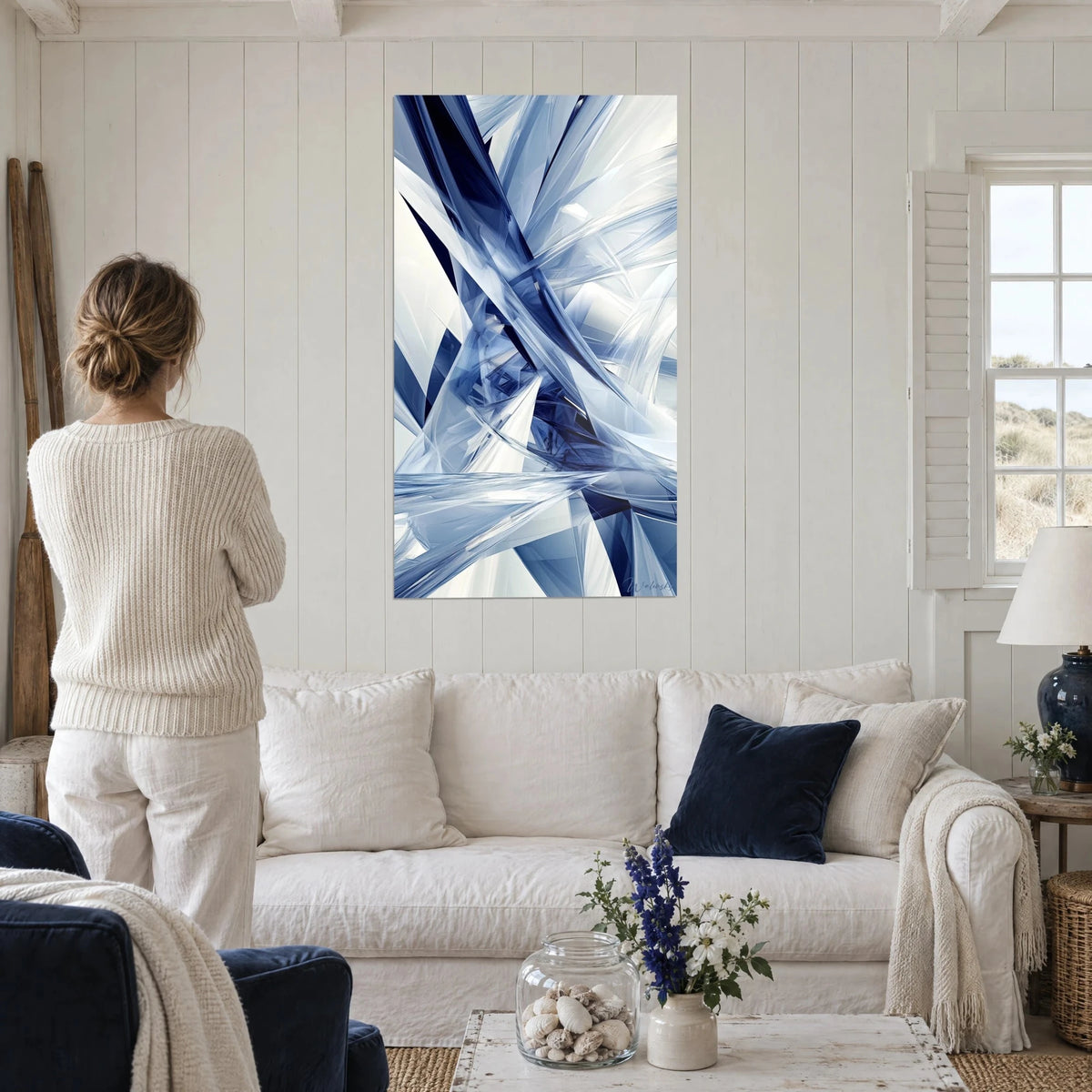 Schilderij met scherven nachtblauw kristal en berijpt wit, vrouw van achteren in crèmekleurige trui, boven een bank in een lichte woonkamer
