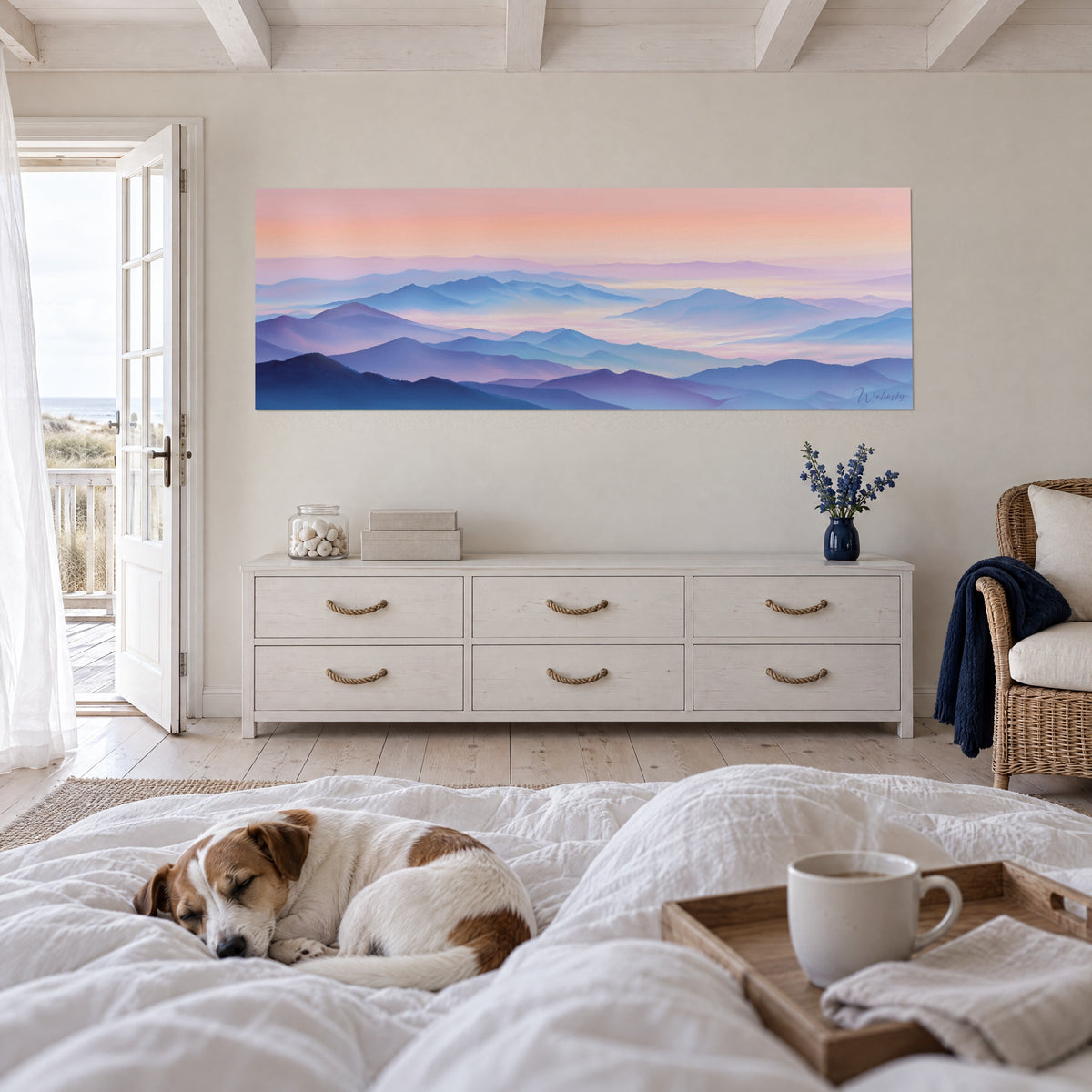 Wall art of a pastel mountain range under a peach sky, a sleeping terrier on the duvet, above a bed in a bright bedroom