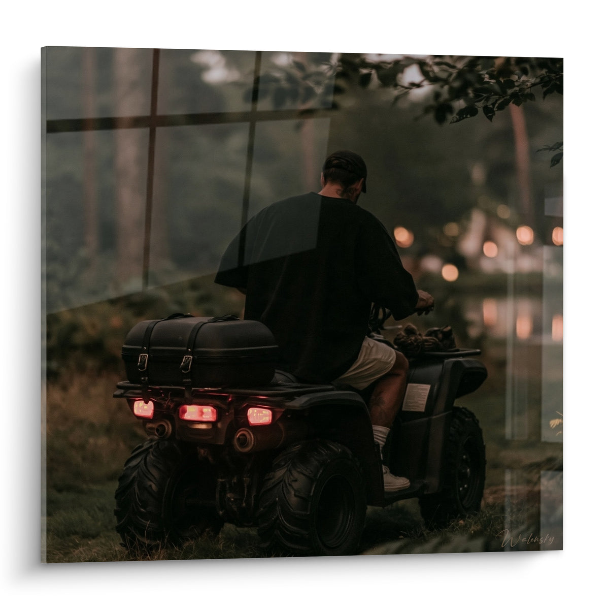 Quad anthracite conduit par un homme de dos, feux rouges allumés dans une forêt ocre au crépuscule