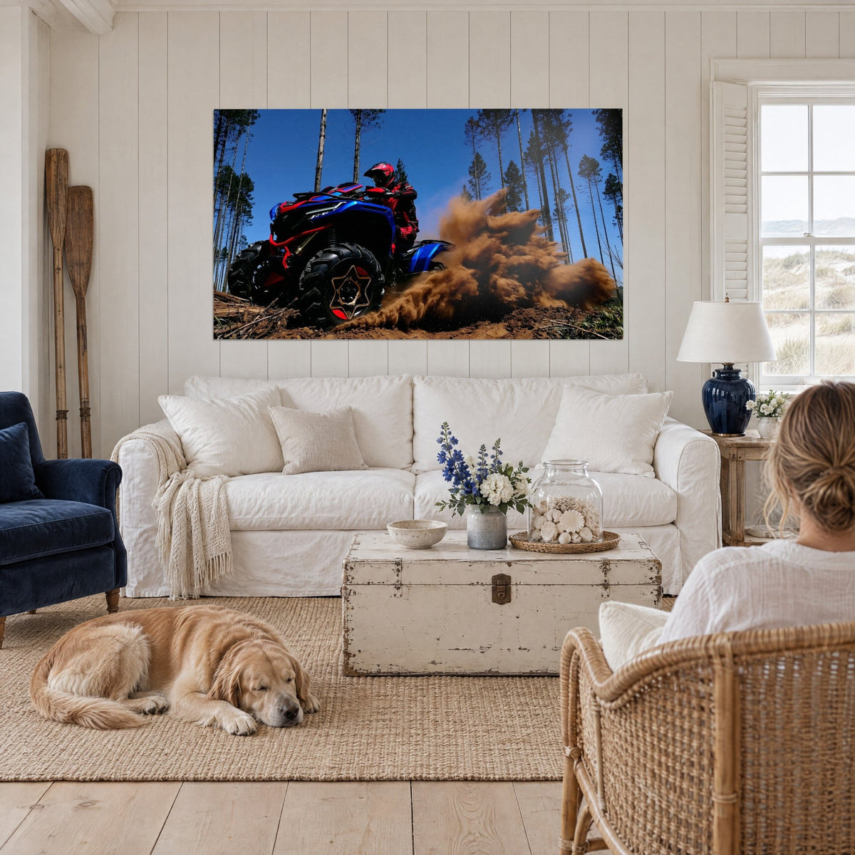 Wall art blue quad bike kicking up a spray of ochre earth, azure sky and pines, above a sofa in a bright living room