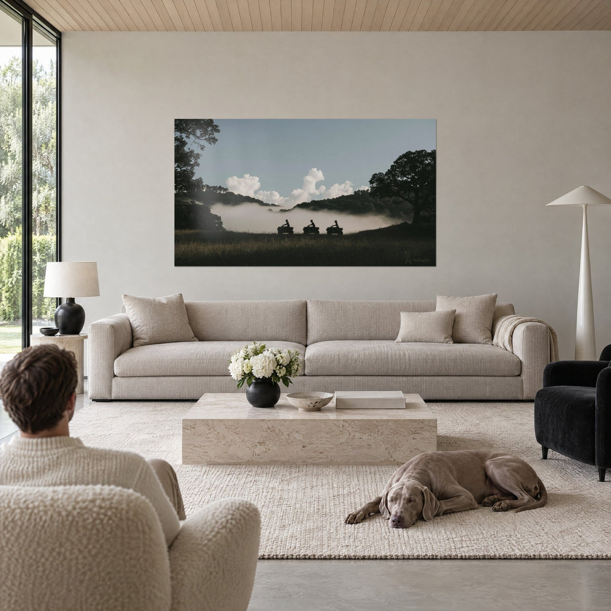 Wall art three quad bikes in black silhouette on a meadow, white mist and pale blue sky, above a sofa in a bright living room