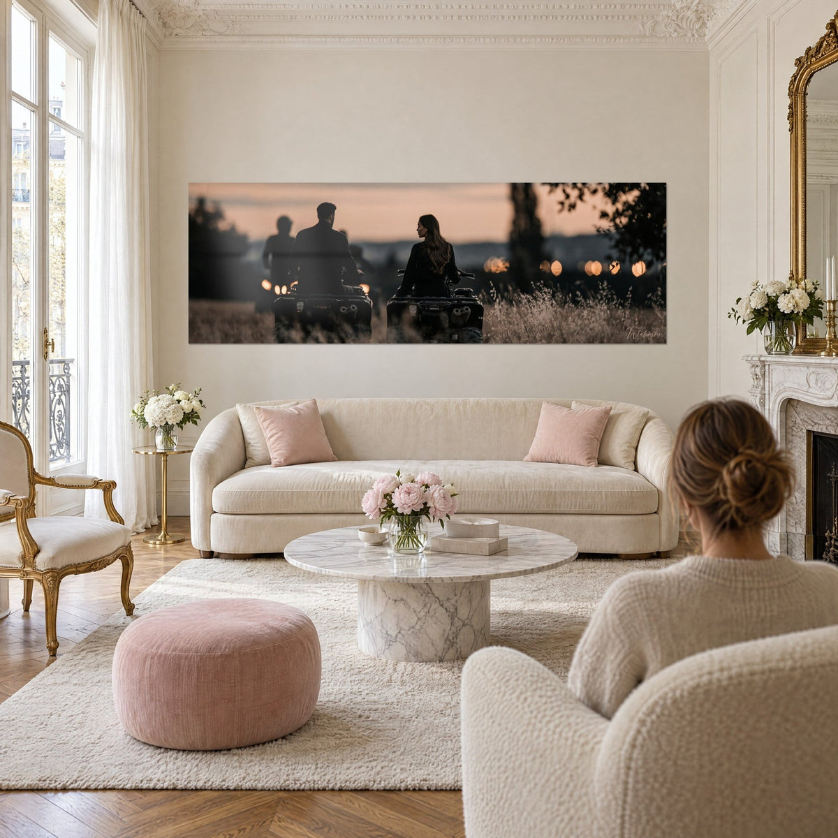 Wall art couple seen from behind on two quad bikes at orange and charcoal dusk, golden grasses, above a sofa in a bright living room