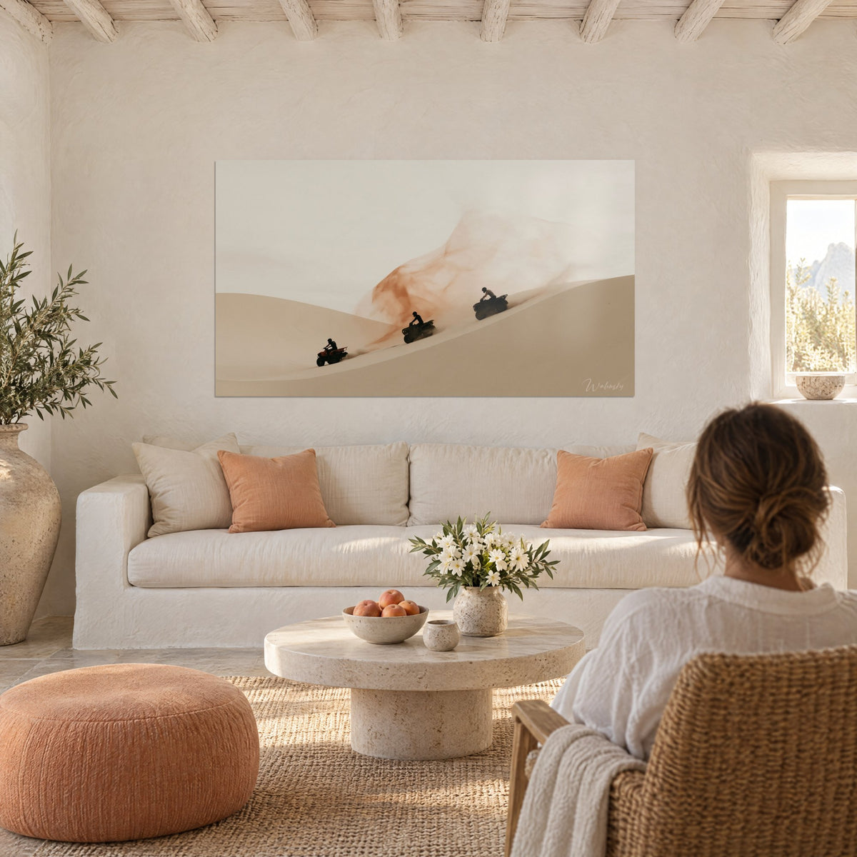 Wall art three quads racing down a beige dune, cloud of orange dust, cream wall, above a sofa in a bright living room