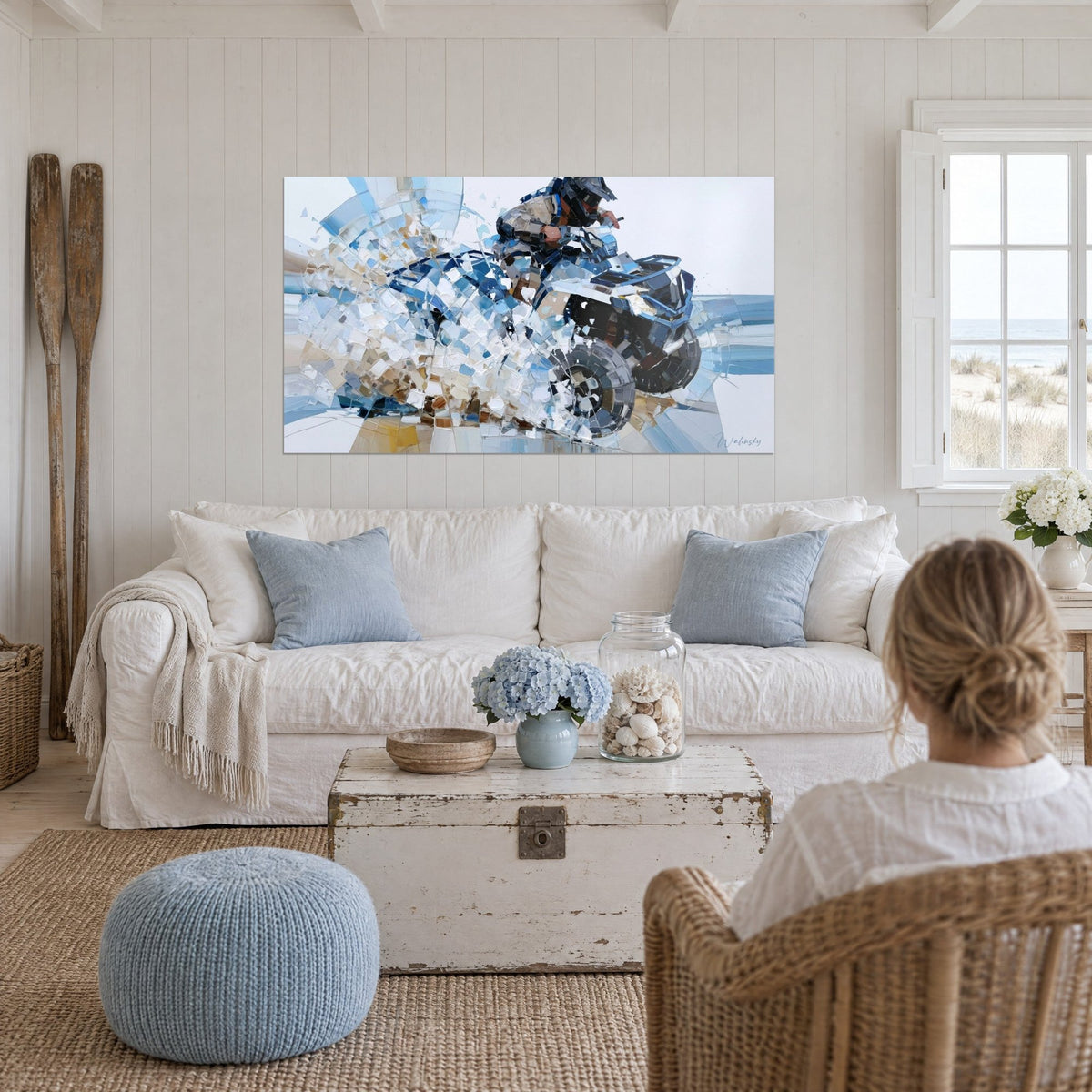 Wall art helmeted quad rider on a navy blue quad, white and beige splashes, above a sofa in a bright living room