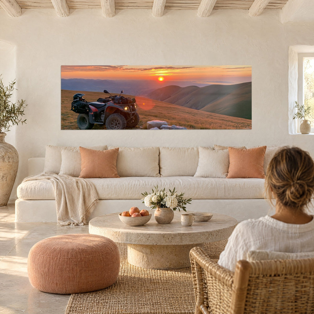 Wall art of a black quad bike parked on a grassy ridge, orange sun and bluish hills, above a sofa in a bright living room