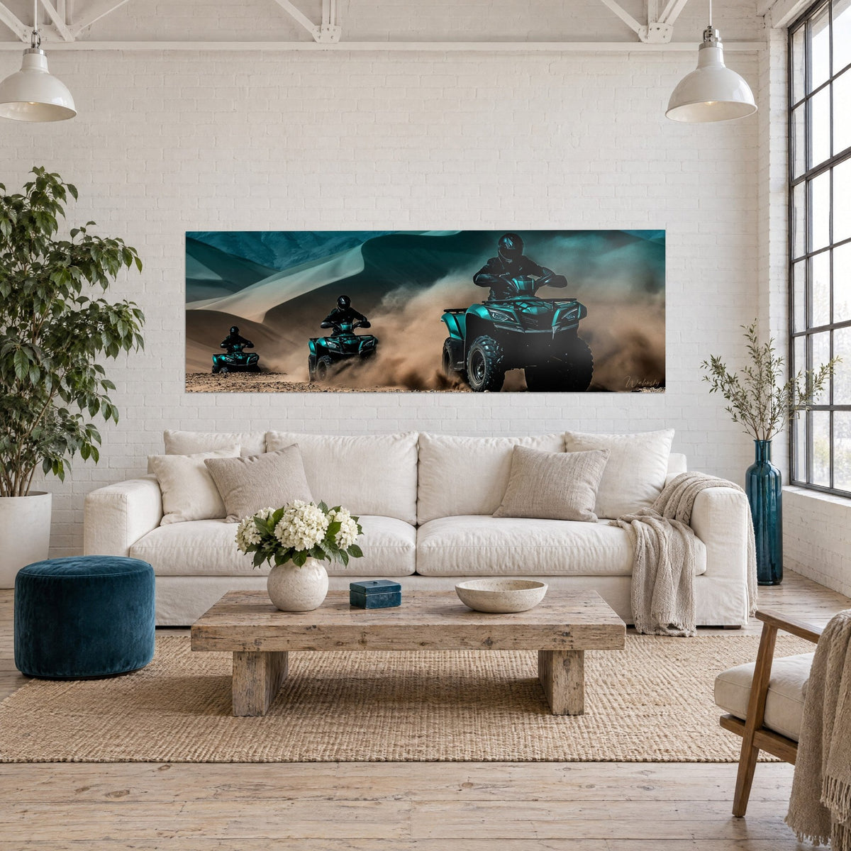 Wall art trio of turquoise quad bikes racing through ochre dust in front of blue-grey dunes, above a sofa in a bright living room