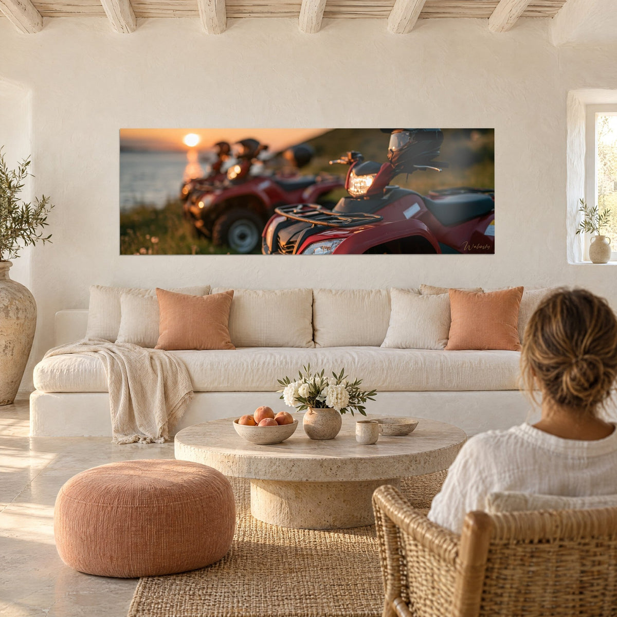 Wall art of red quad bikes lined up facing the sea, orange sun in the distance, woman seen from behind, above a sofa in a bright living room
