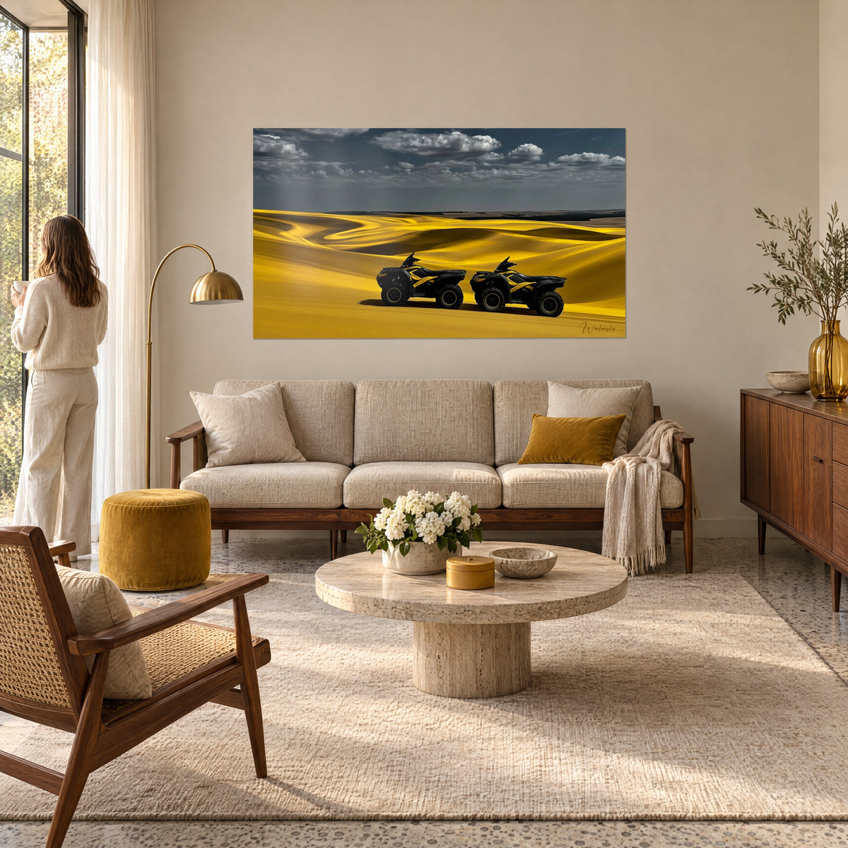 Wall art two black quad bikes with yellow stripes on golden dunes, stormy grey-blue sky, above a sofa in a bright living room