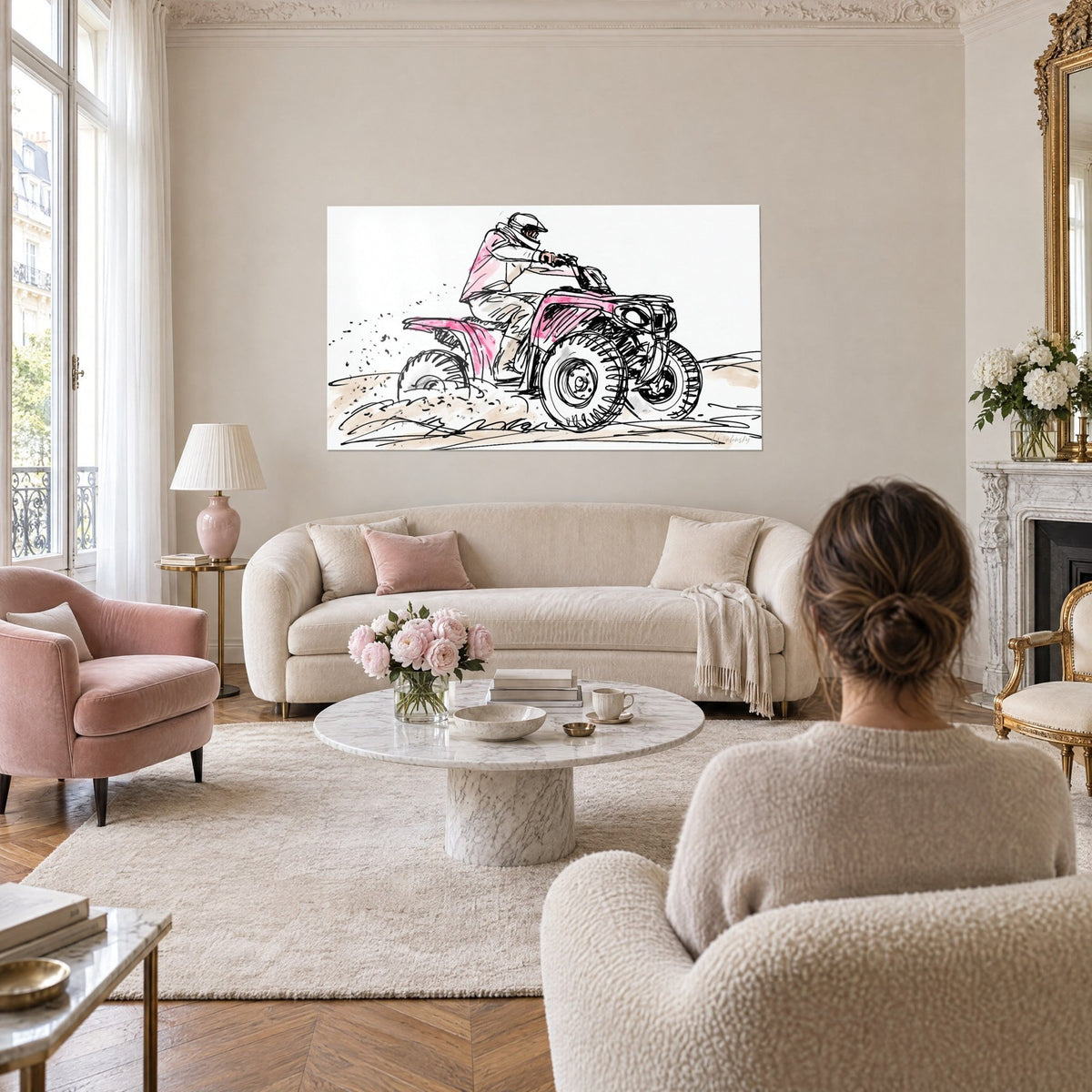 Wall art of a quad kicking up dust, helmeted rider in a pink jacket, black sketch and sand, hung above a sofa in a bright living room