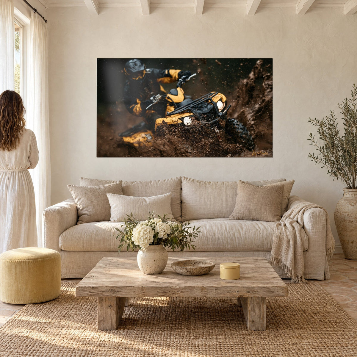 Wall art yellow and black quad bike plowing through mud, helmeted rider, brown clods flying, above a sofa in a bright living room
