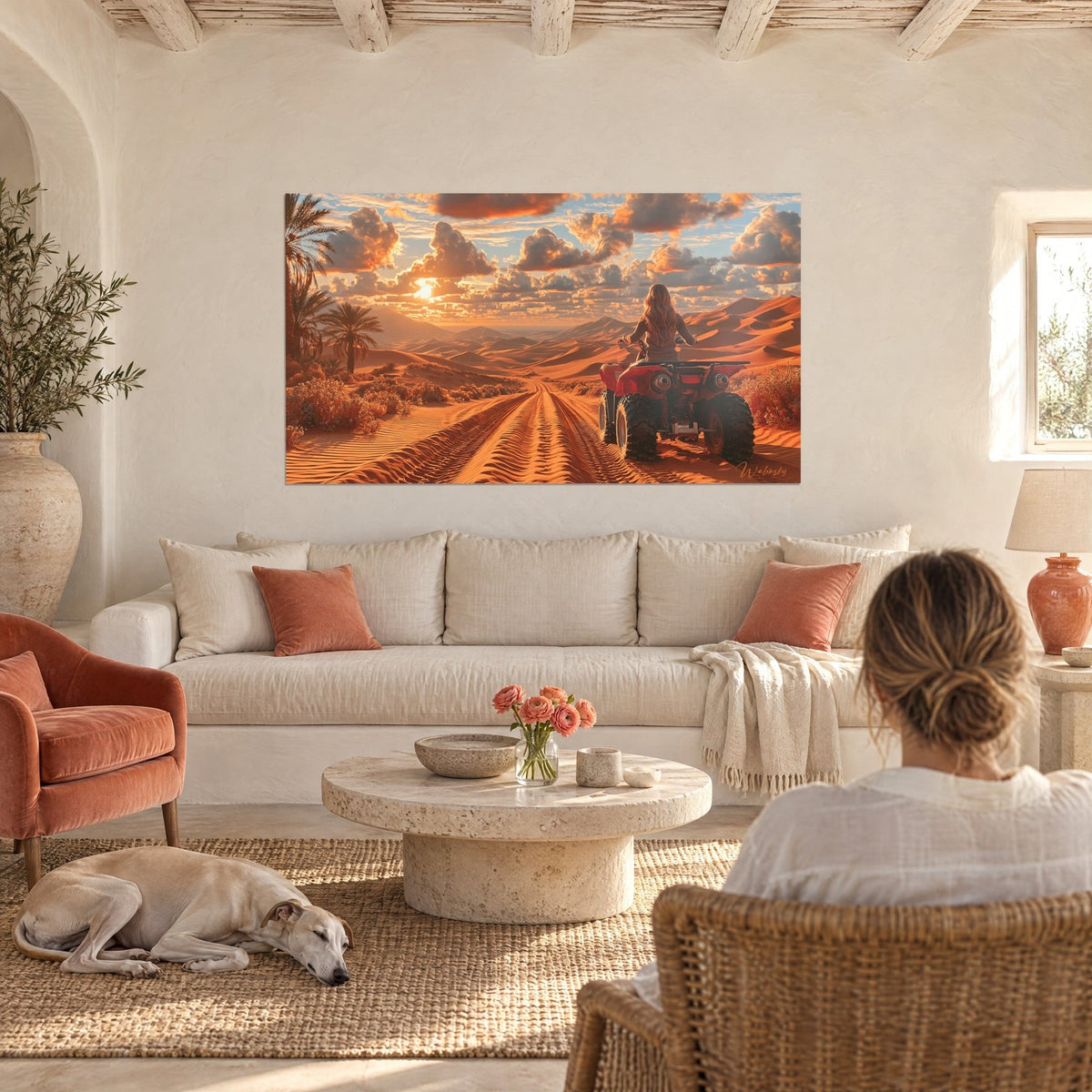 Tableau quadriste aux cheveux ondulés face aux dunes orangées et nuages rosés, au-dessus d'un canapé dans un salon lumineux