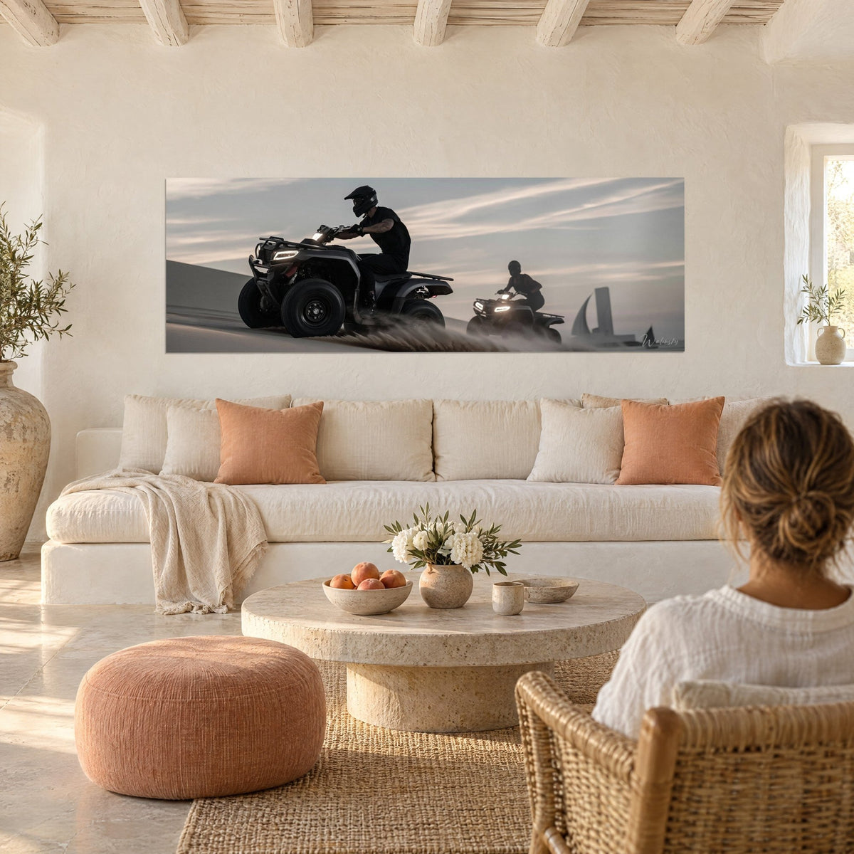 Wall art black quad kicking up sand, helmeted rider and grey-pink twilight glow, above a sofa in a bright living room