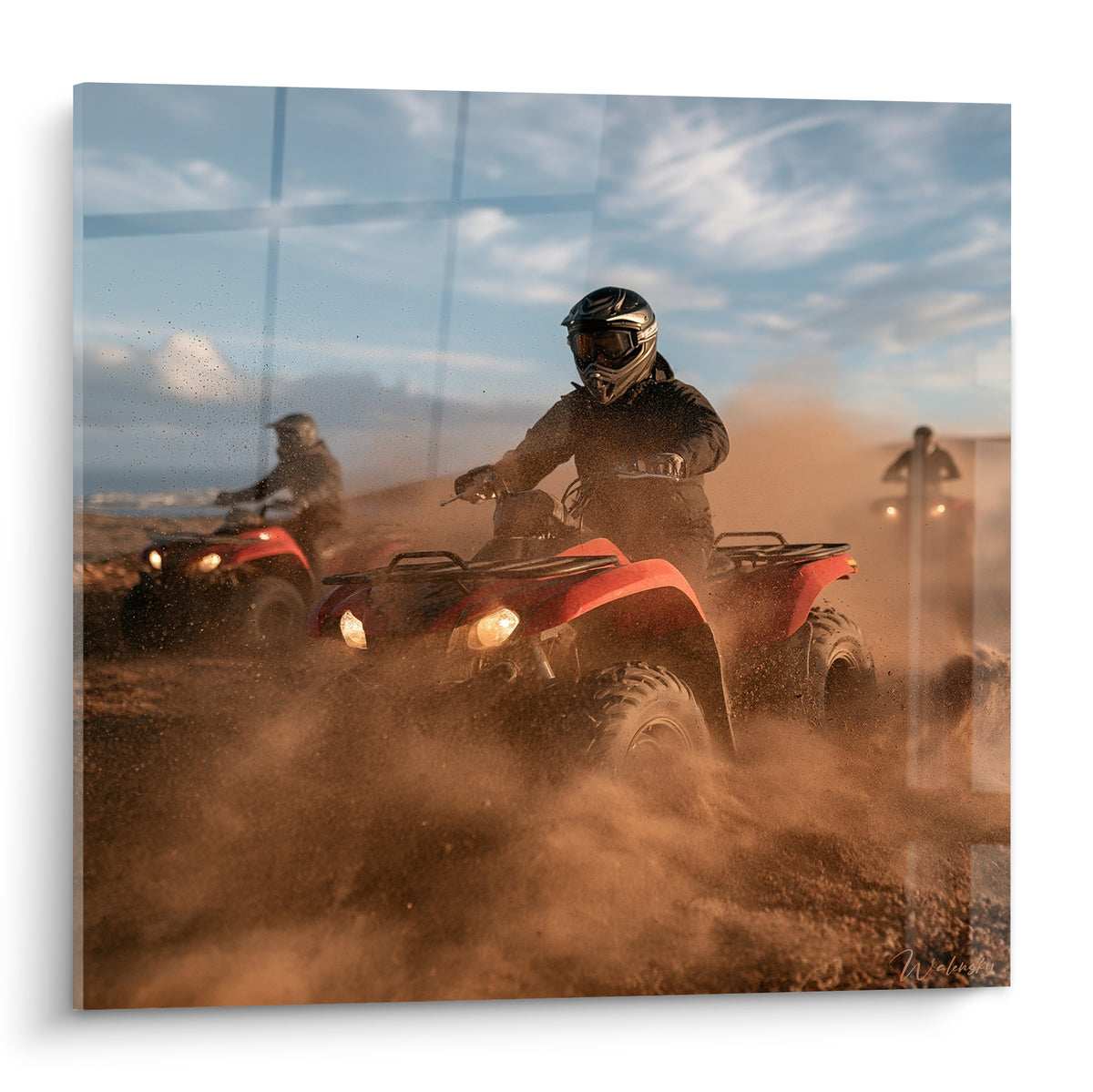 Quad rouge fonçant dans une poussière ocre sous un ciel bleu marbré de nuages blancs