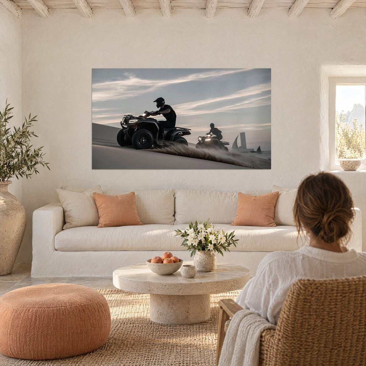 Wall art of black quads racing across a dune at dusk, blue-grey sky streaked with white, ivory wall above a sofa in a bright living room