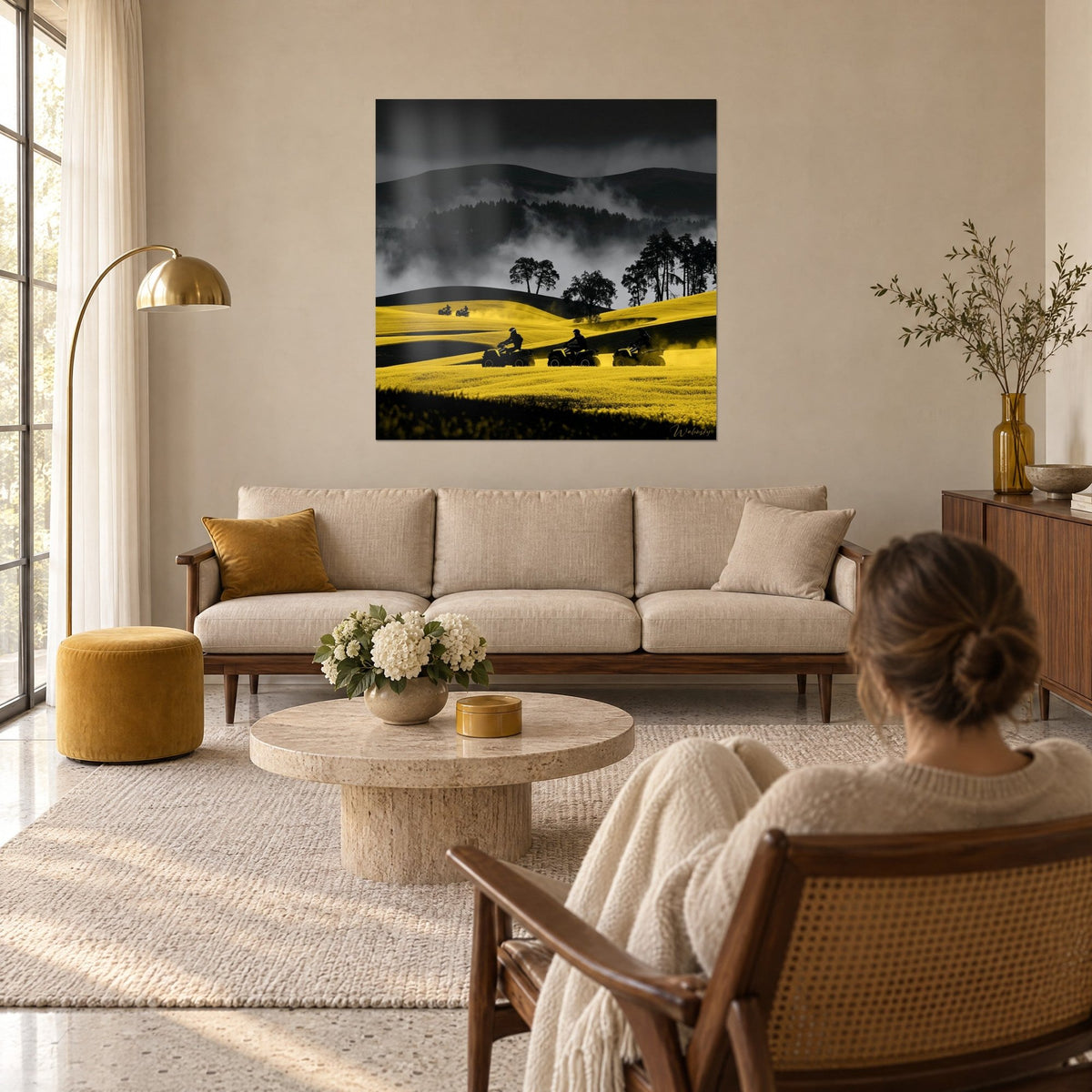 Wall art three black quads racing over yellow rapeseed hills, grey mist in the background, above a sofa in a bright living room