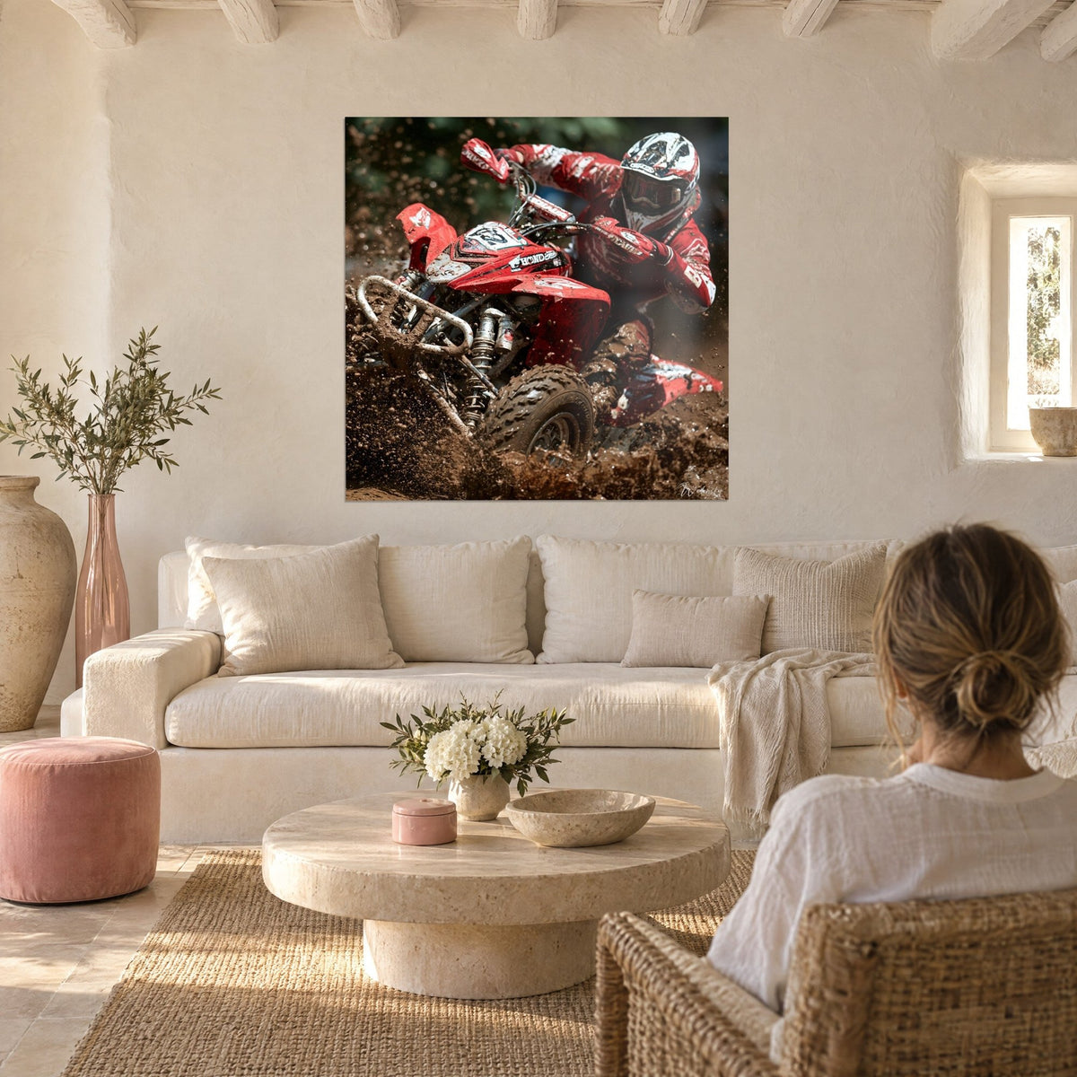 Wall art of a quad pilot in a white and red helmet tearing through brown mud, spatters above a sofa in a bright living room